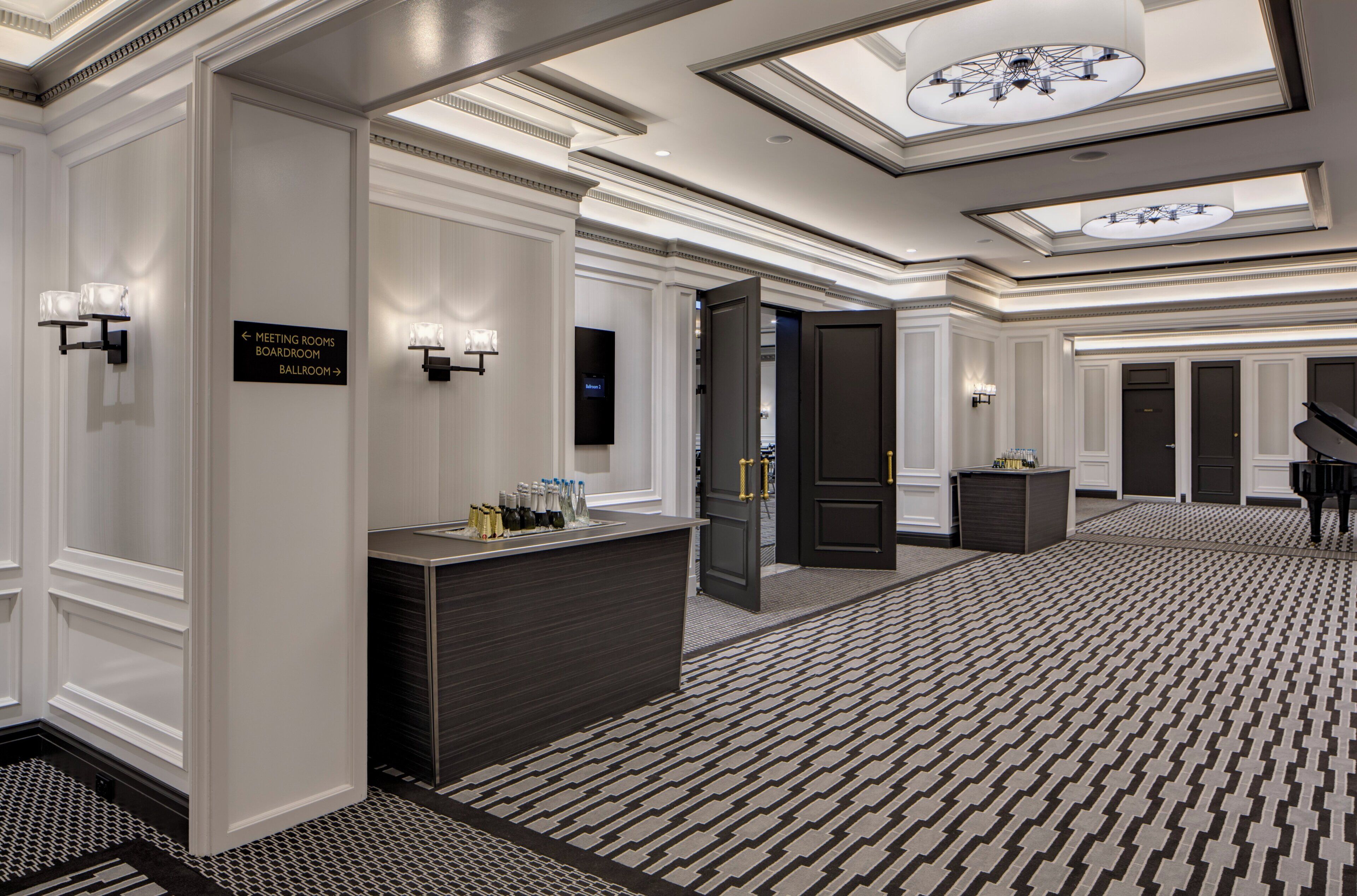 A hotel lobby with a reception desk, directional signage, a chandelier, and a patterned carpet.