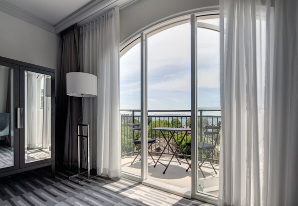 A modern hotel room with a large sliding glass door leading to a balcony with outdoor furniture.