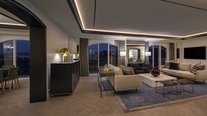 Una sala de estar moderna con sofá, mesa de centro y sillas. Hay un ventanal con vista a la ciudad de noche.