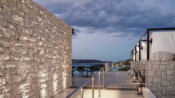 A stone wall with a metal railing, outdoor seating, and a view of the sea.