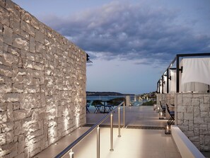 Un muro de piedra con barandilla metálica, asientos al aire libre y vista al mar.