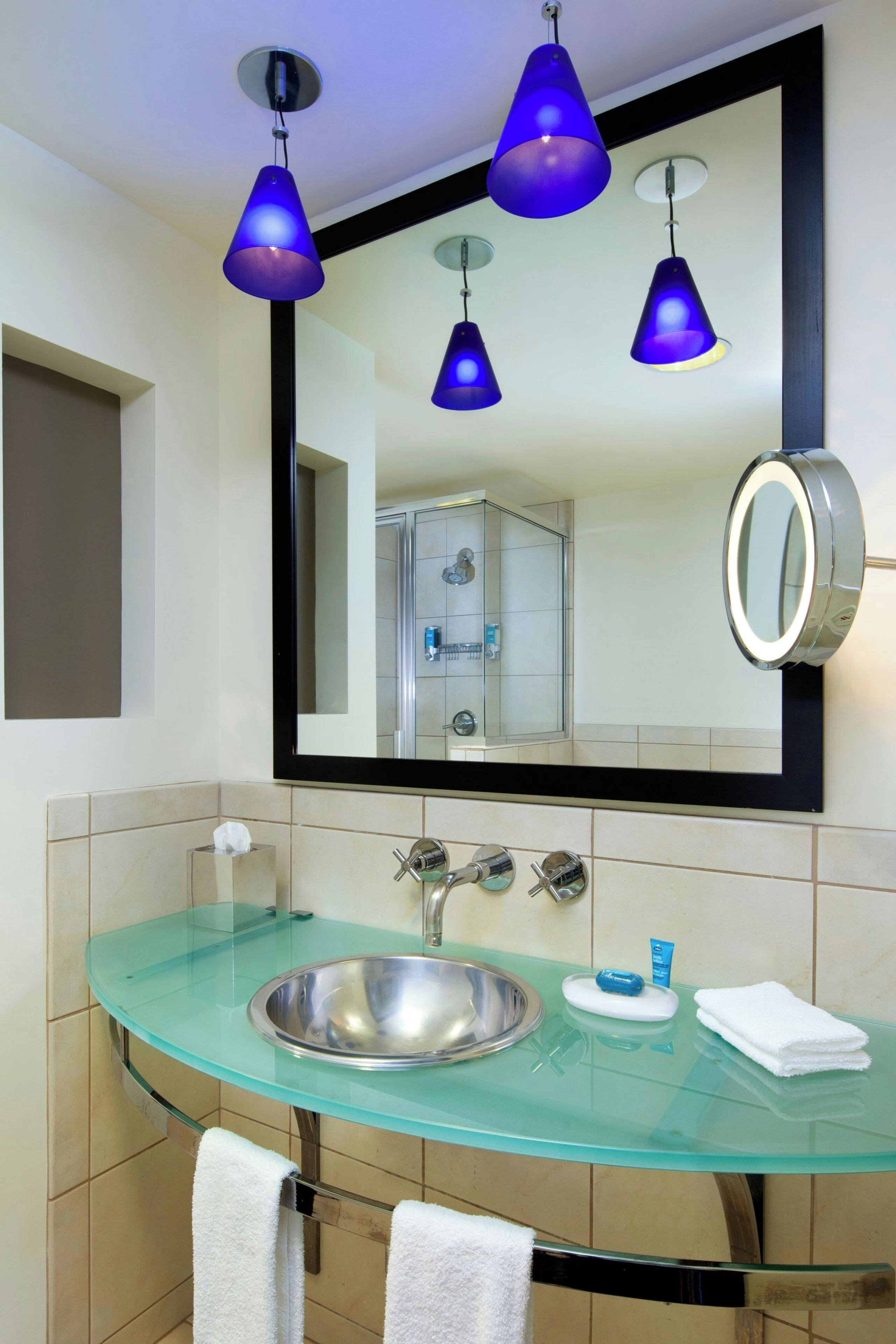 A bathroom with a glass sink, a mirror, and three blue pendant lights.