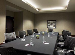 A conference room with a long table, black chairs, water bottles, and a framed botanical print on the wall.