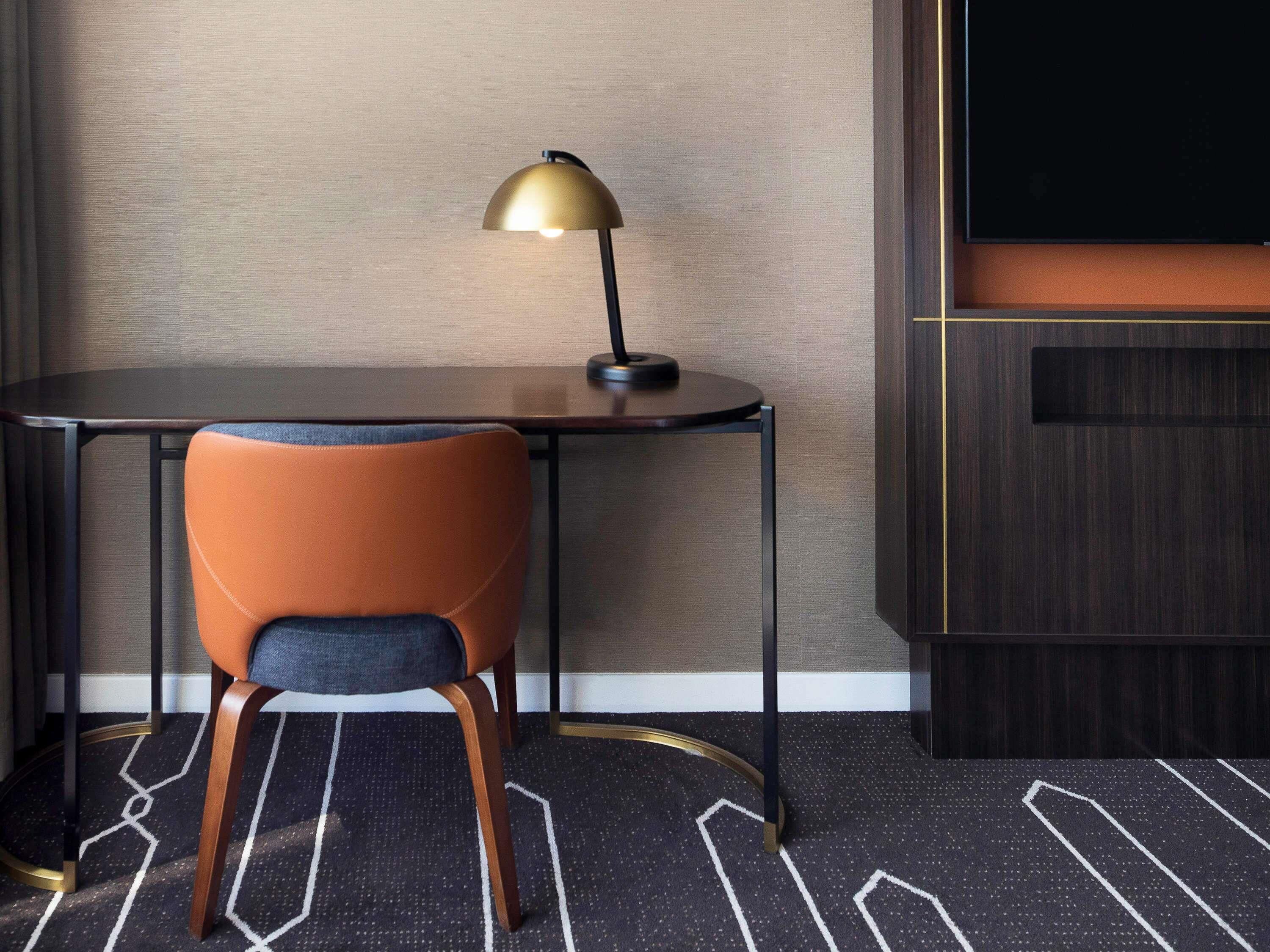 Habitación de hotel con un escritorio de madera oscura, una silla, una lámpara dorada y un televisor de pantalla plana grande.