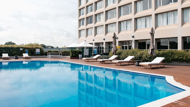 A hotel with a swimming pool, sun loungers, and a large building with multiple windows. - Mercure Sydney Parramatta (Rosehill)