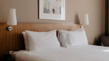 Habitación de hotel con una cama, dos lámparas fijadas a la pared, un cuadro sobre la cama y un cabecero de madera.