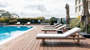 A poolside area with lounge chairs and umbrellas, a wooden deck, and a building in the background. - Mercure Sydney Parramatta (Rosehill)