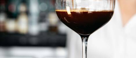 A martini glass filled with a dark liquid, likely a cocktail, being poured from a bottle.