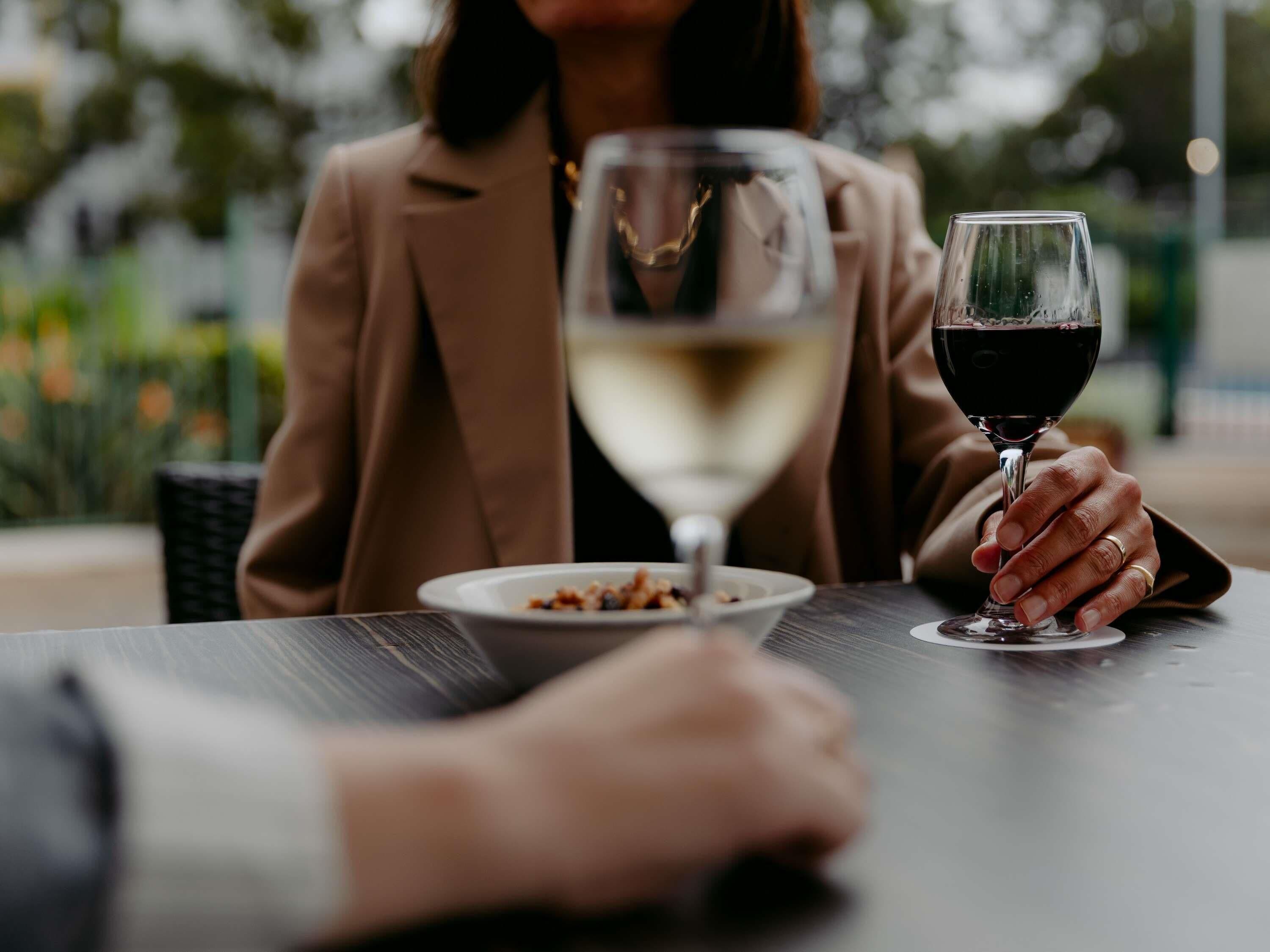 A person sitting at an outdoor table with a wine glass and a plate of food.