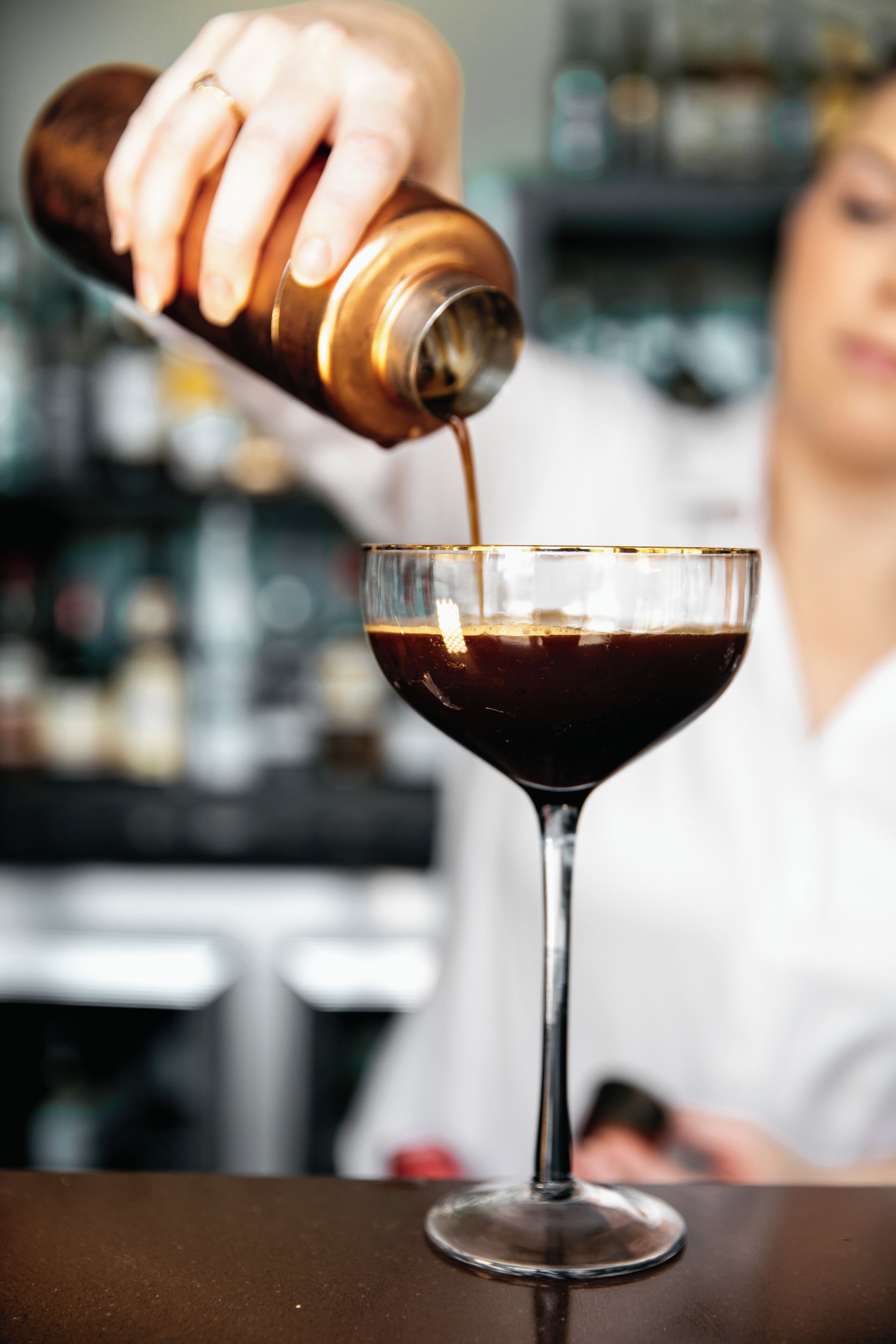 Una mà abocant un líquid fosc a una copa de martini.