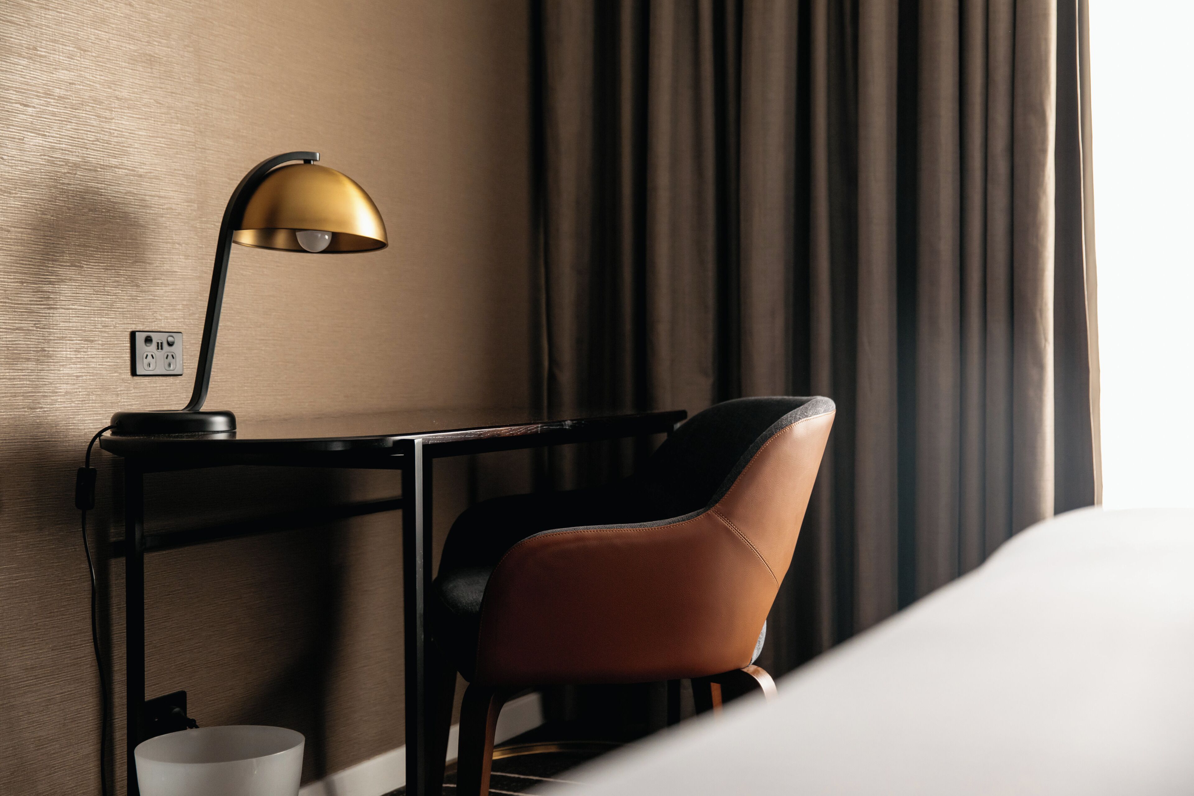 A hotel room with a desk, a chair, a lamp, and a bed.