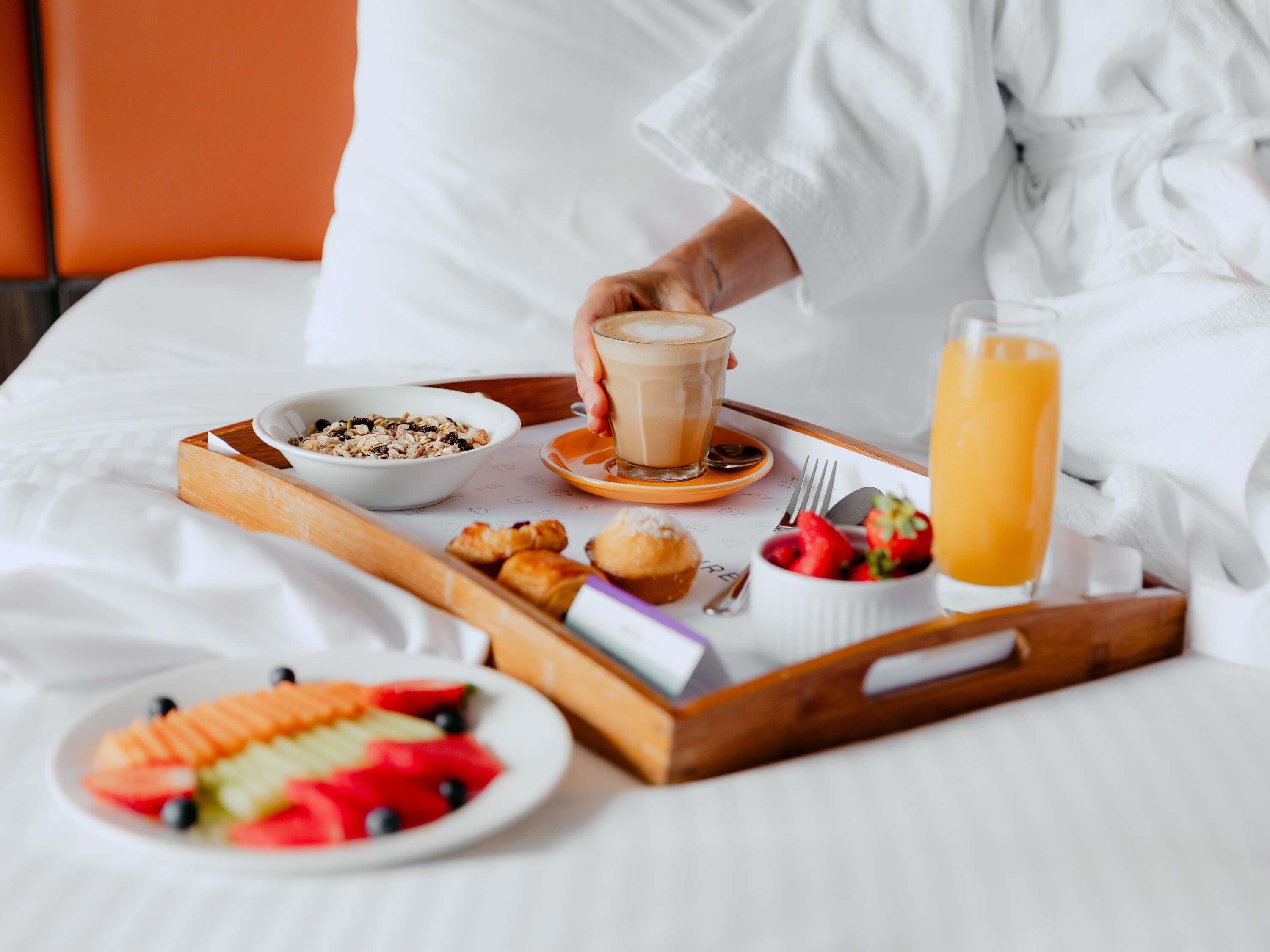 A breakfast tray with cereal, croissants, strawberries, and a glass of orange juice on a bed.