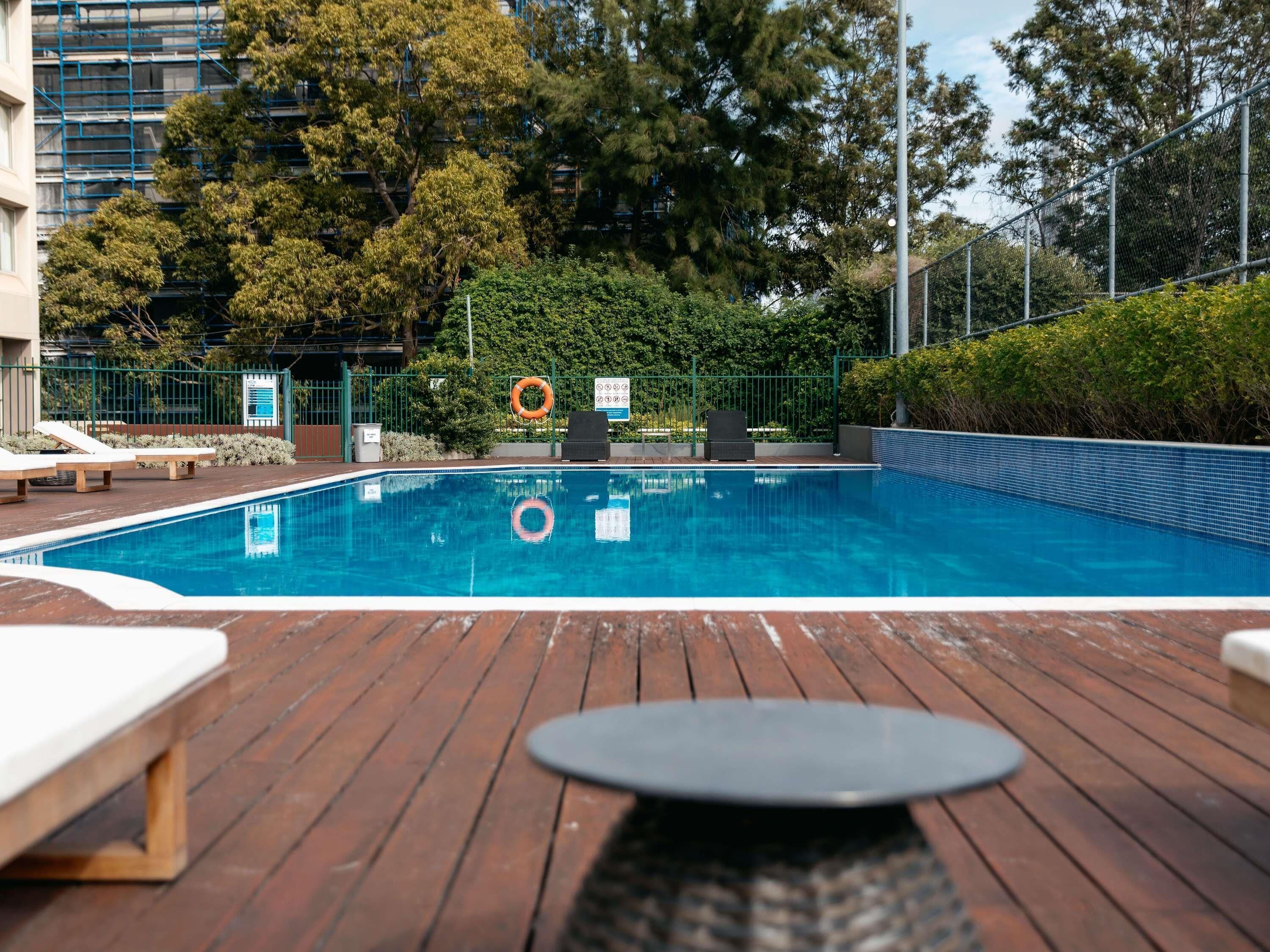 Una piscina con sillas de descanso y un flotador salvavidas, rodeada de árboles y una valla.