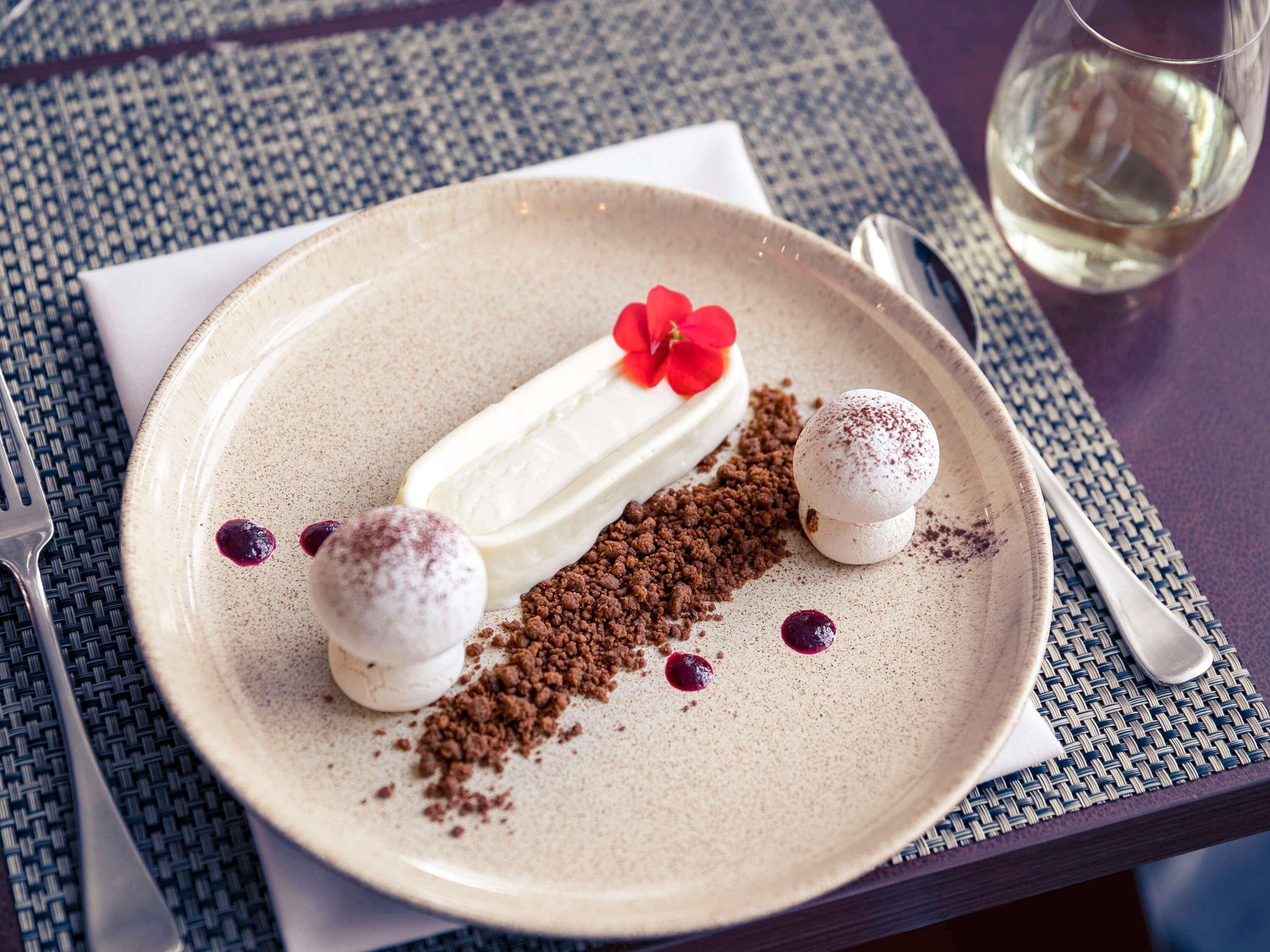 Un plato con un postre de chocolate, dos dulces esféricos y una flor decorativa sobre un mantel con textura.