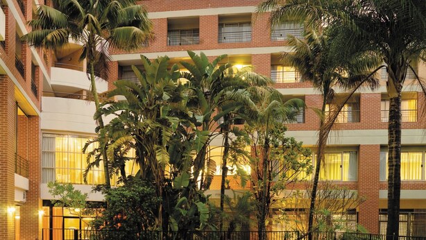 Un hotel con piscina rodeado de palmeras y un edificio de ladrillo con balcones.