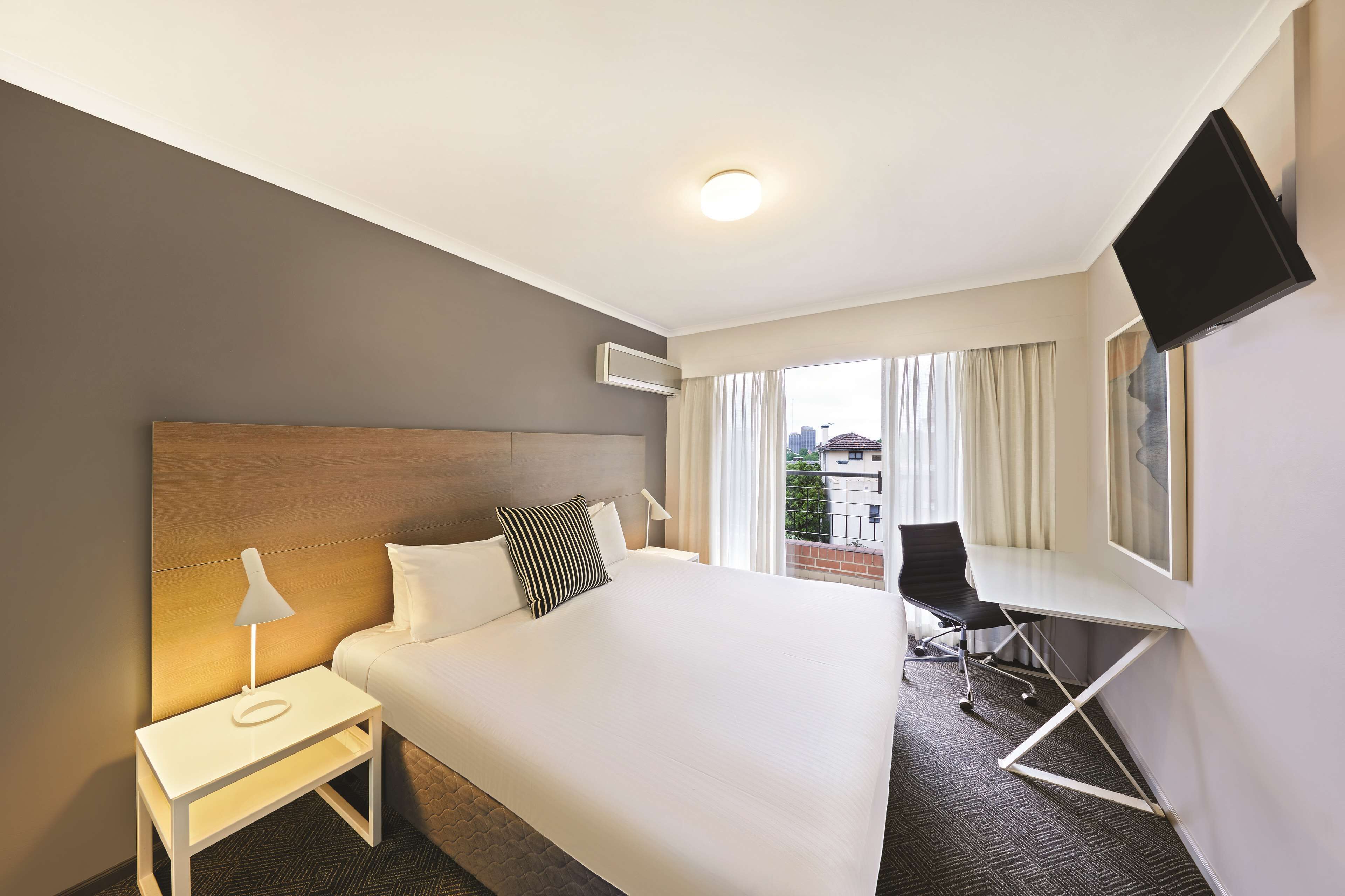 Ein Hotelzimmer mit Bett, Schreibtisch, Stuhl, Fernseher und einem Fenster mit Vorhängen.