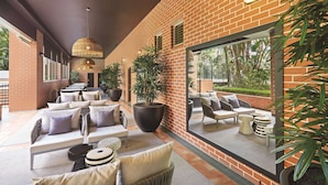 Un espacio lounge moderno al aire libre, con paredes de ladrillo, plantas grandes en macetas y asientos cómodos.