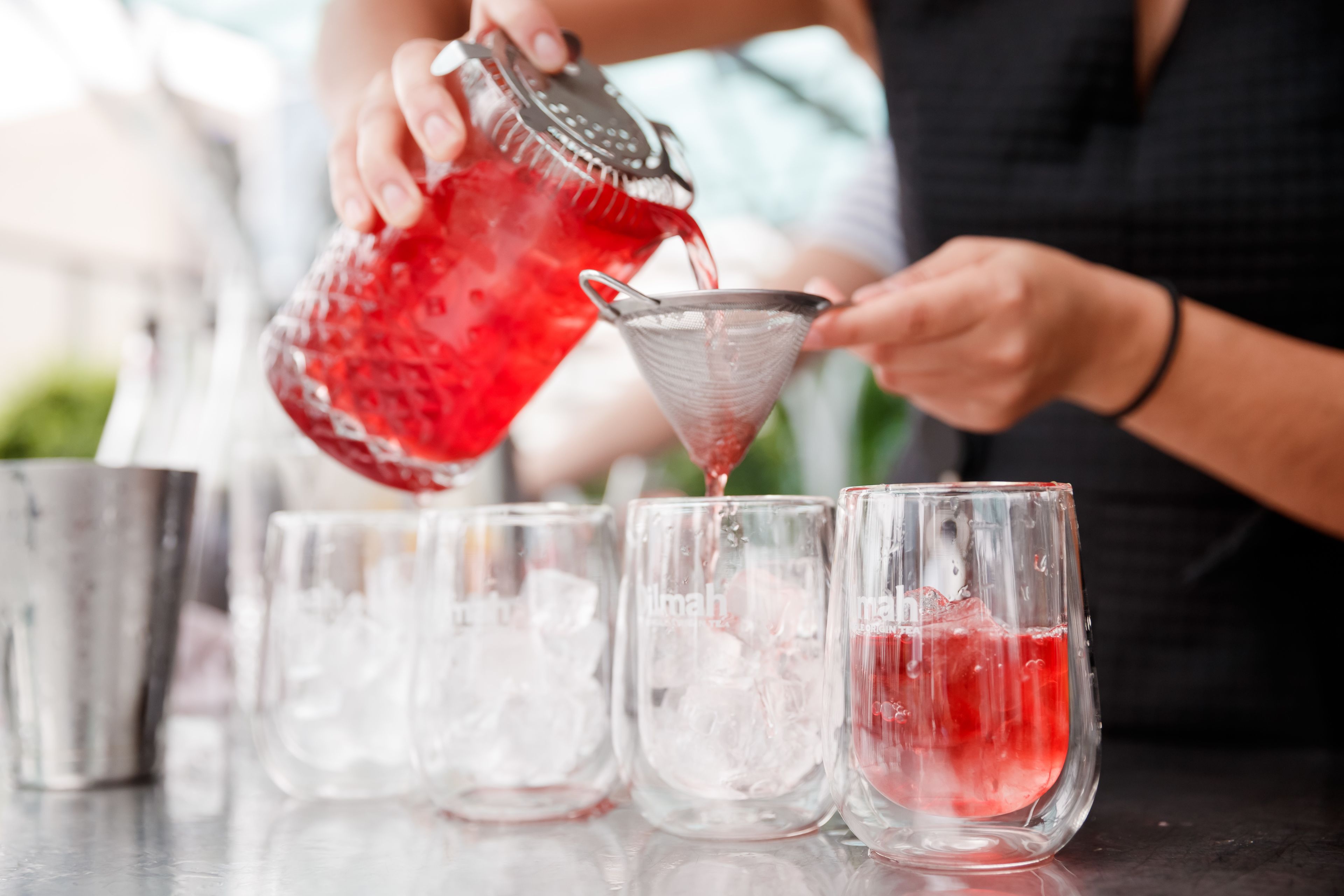 A person pouring a red liquid into a glass with a metal strainer.