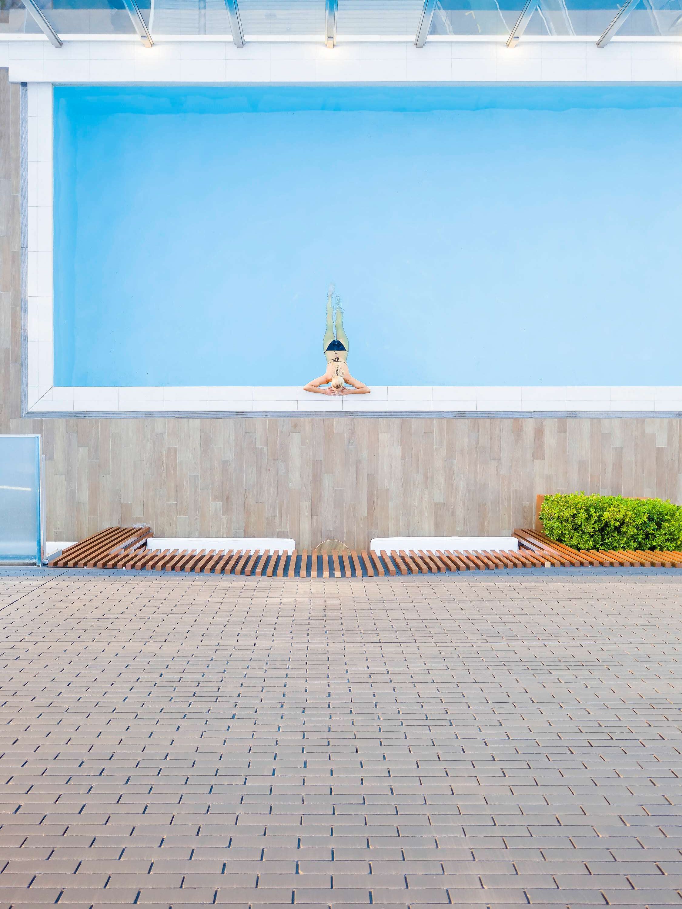 A swimming pool with a clear blue sky in the background, a wooden deck area, and a hedge.