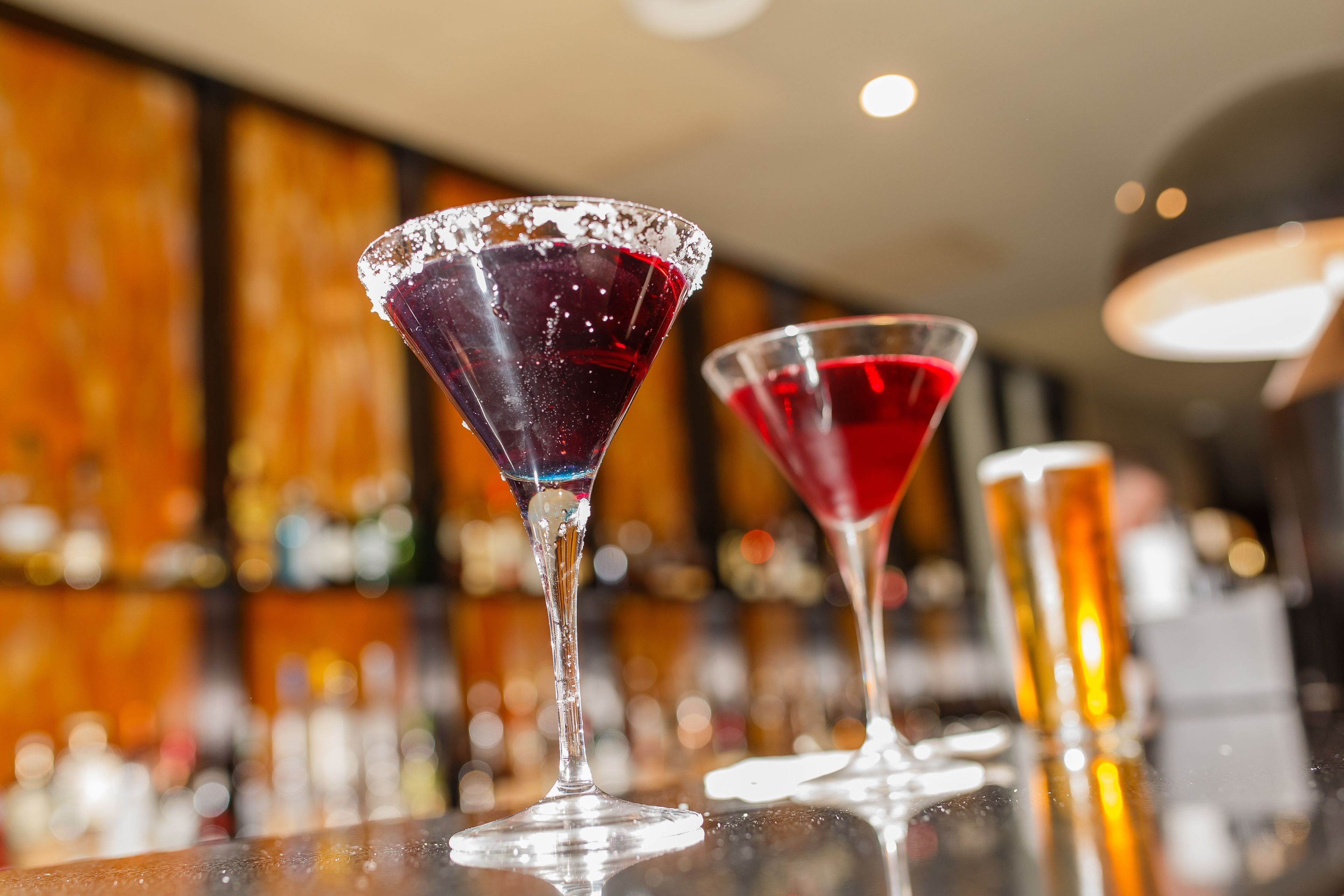 Two martini glasses on a bar counter with a blurred background of bottles.
