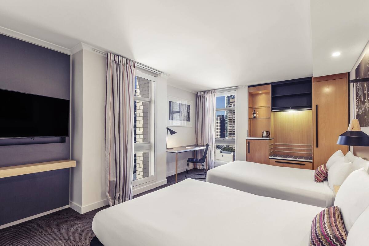 A hotel room with a large bed, a desk, a TV, and a view of the city.