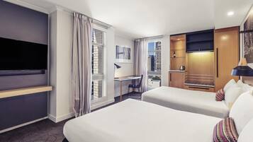 Habitación de hotel con una cama grande, un escritorio, un televisor y vistas a la ciudad.