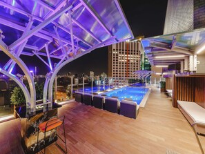 A rooftop pool area with a glass balustrade, lounge chairs, and a view of the city skyline at night. - Mercure Brisbane King George Square (Brisbane)