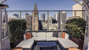 A rooftop lounge with a city view, a large sectional sofa, and two small round tables. - Mercure Brisbane King George Square (Brisbane)