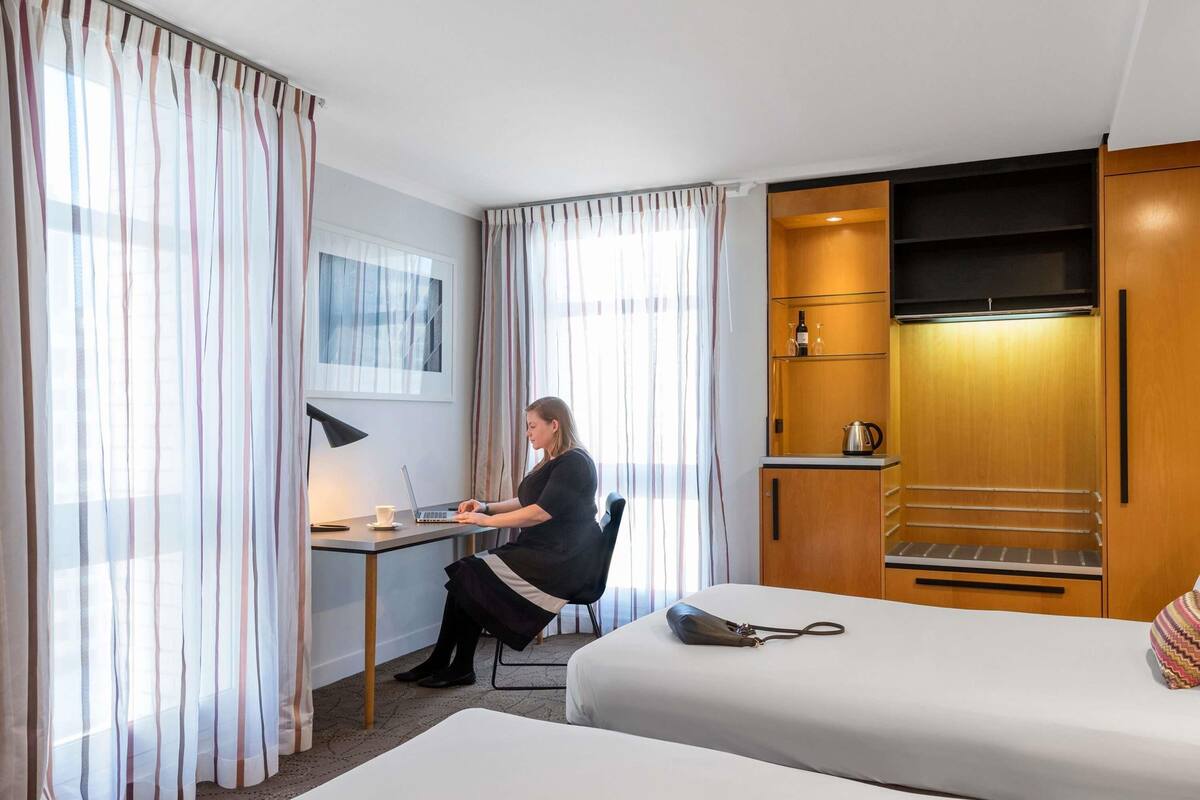 A hotel room with a desk, two beds, a minibar, and a TV.