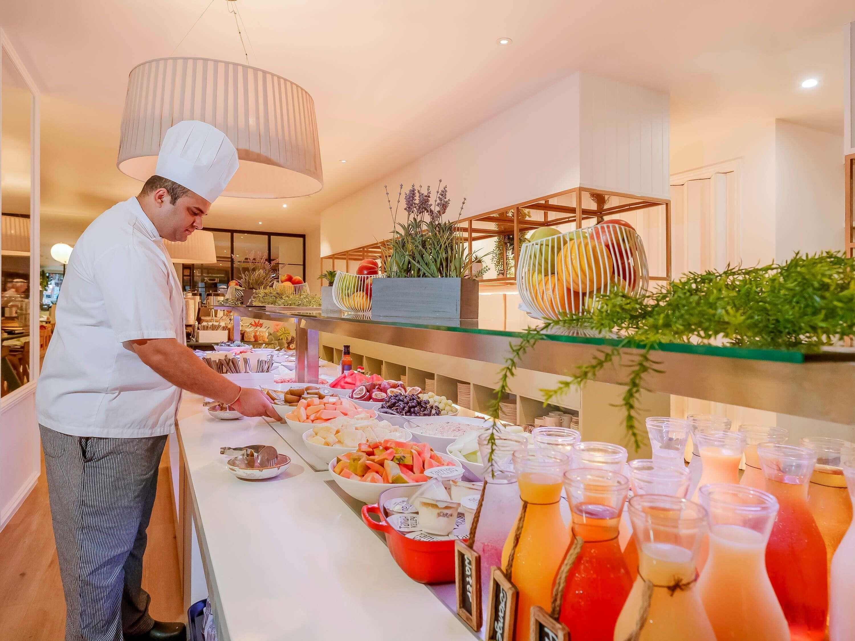 Montaje de bufé con un chef preparando alimentos, diversas frutas y bebidas a la vista.