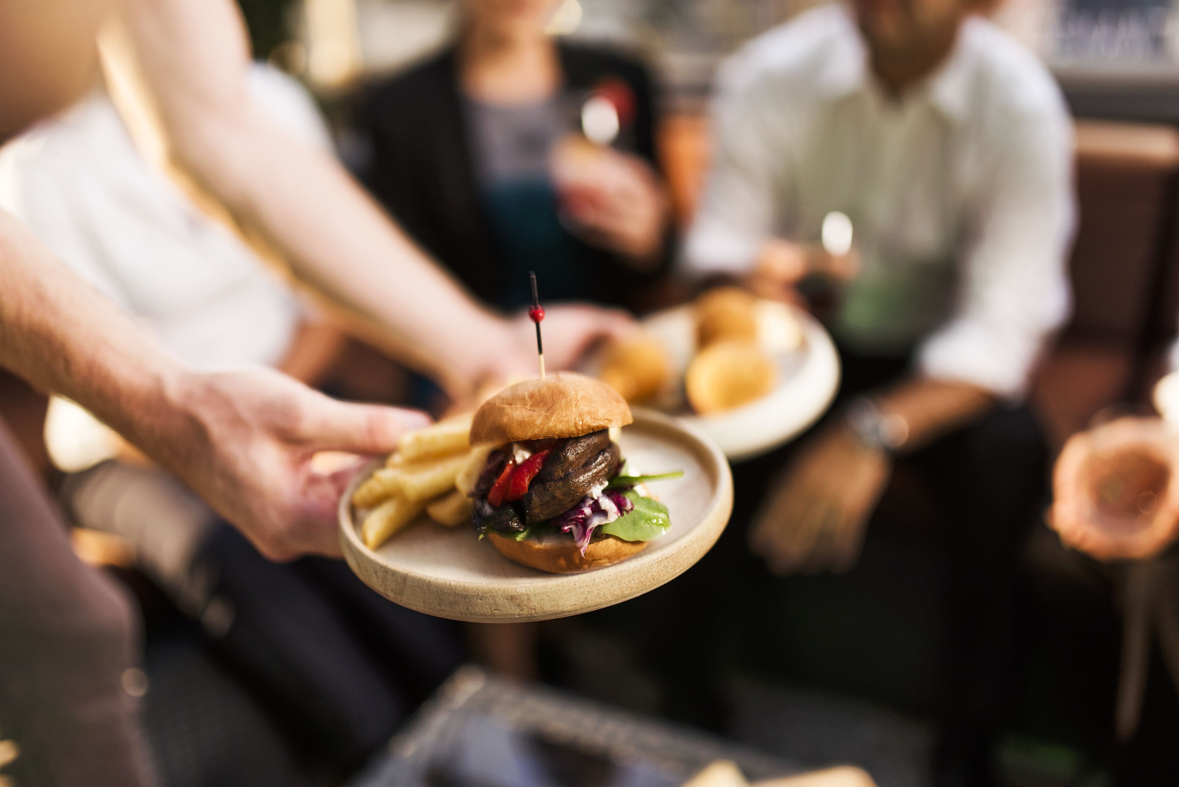 Una persona sosteniendo un plato con una hamburguesa y papas fritas.