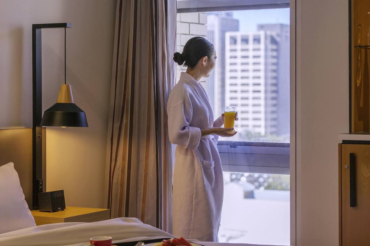 A hotel room with a bed, a tray of breakfast, a lamp, and a view of buildings through the window.