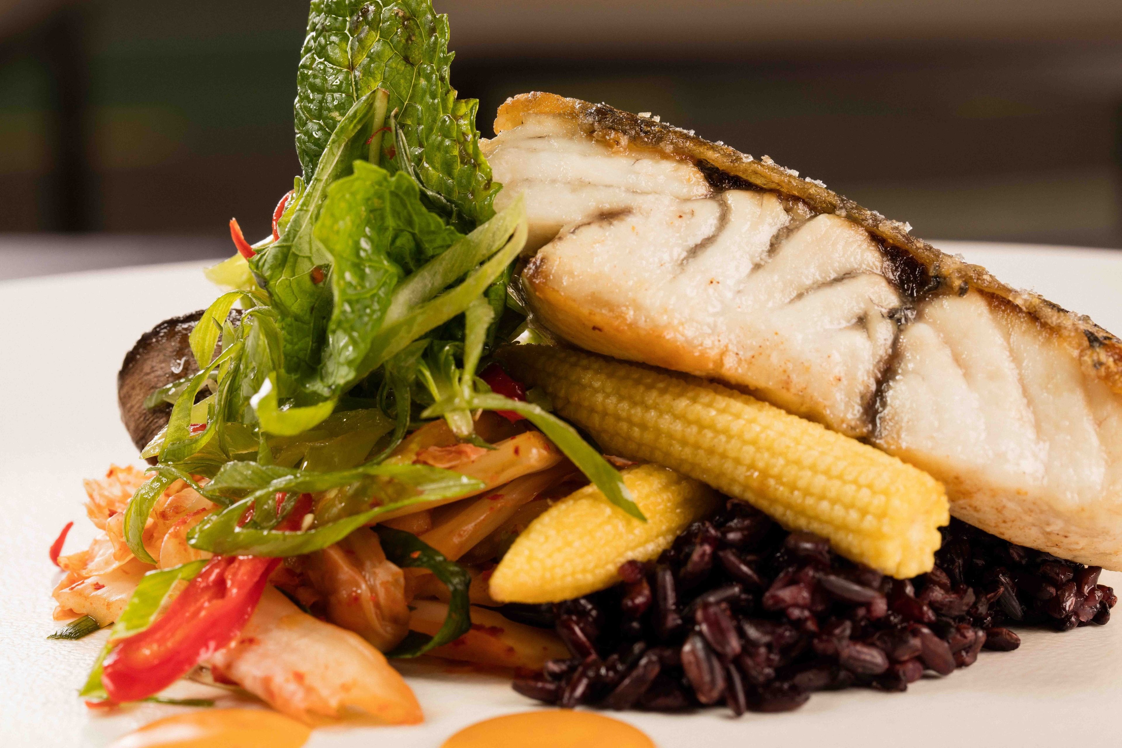 Une assiette de nourriture comprenant du poisson, du maïs et du riz noir.