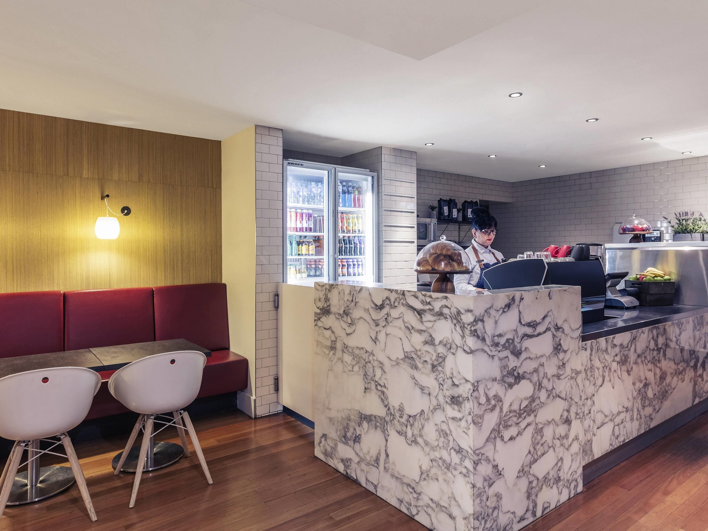 Un restaurante con mostrador de mármol, piso de madera, asientos rojos y un refrigerador lleno de bebidas.