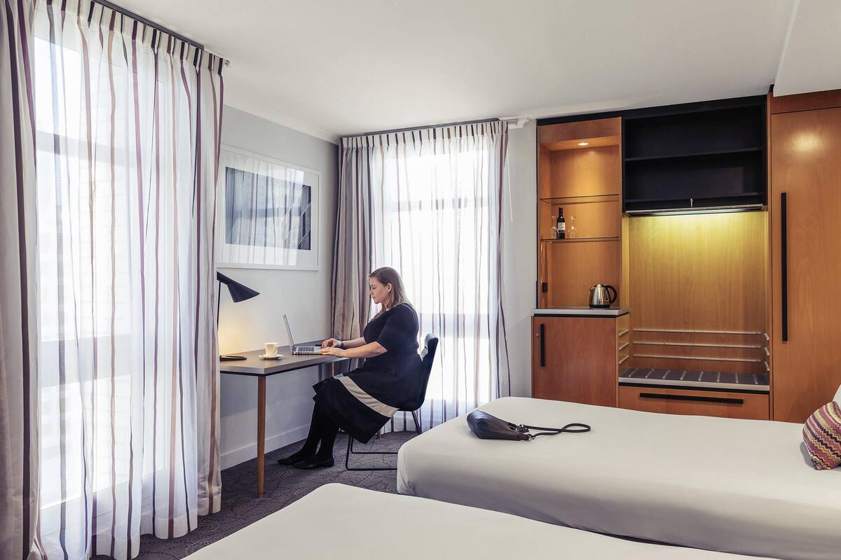 Habitación de hotel con escritorio, laptop, silla, cama, televisor y minibar.