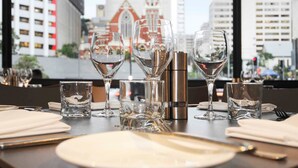A dining table set with wine glasses, a bottle, and cutlery in a restaurant with a city view. - Mercure Brisbane King George Square (Brisbane)