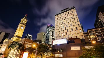 A modern hotel with a prominent clock tower in the background, surrounded by high-rise buildings.