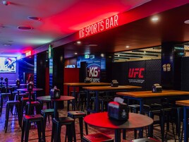 A sports bar with multiple tables and stools, a large screen displaying sports content, and a prominent UFC logo on the wall.