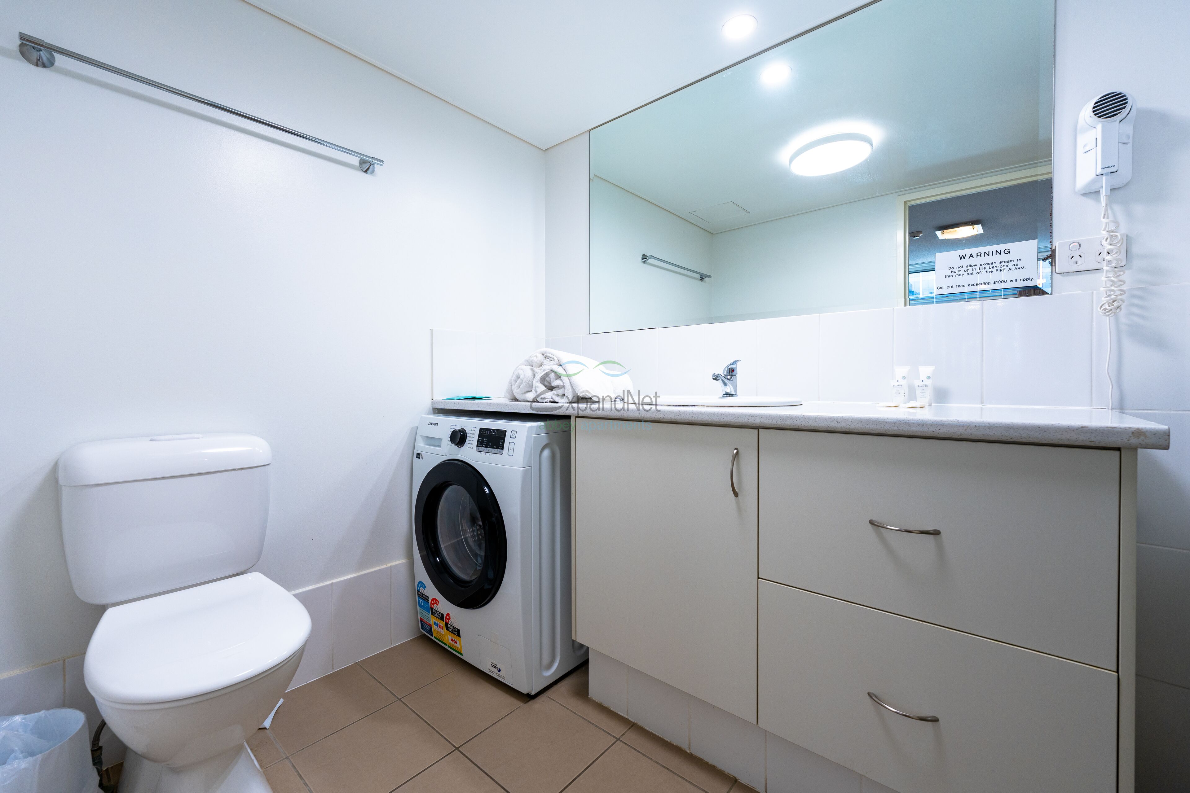 Un baño moderno con inodoro, lavadora y un espejo sobre el lavabo.