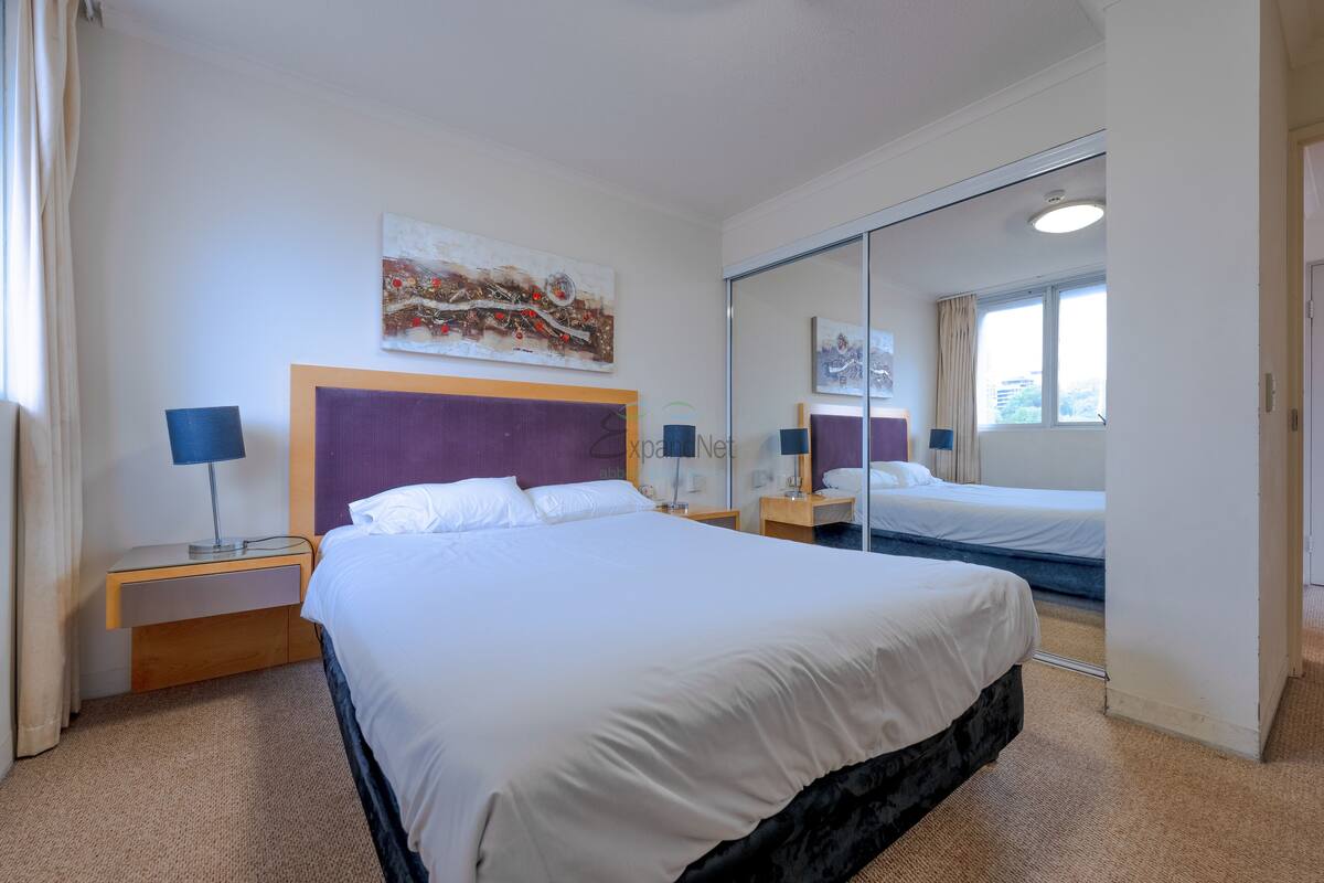 Ein Hotelzimmer mit einem großen Bett, einem Nachttisch mit Lampe, einem Spiegel und einem Bild an der Wand.
