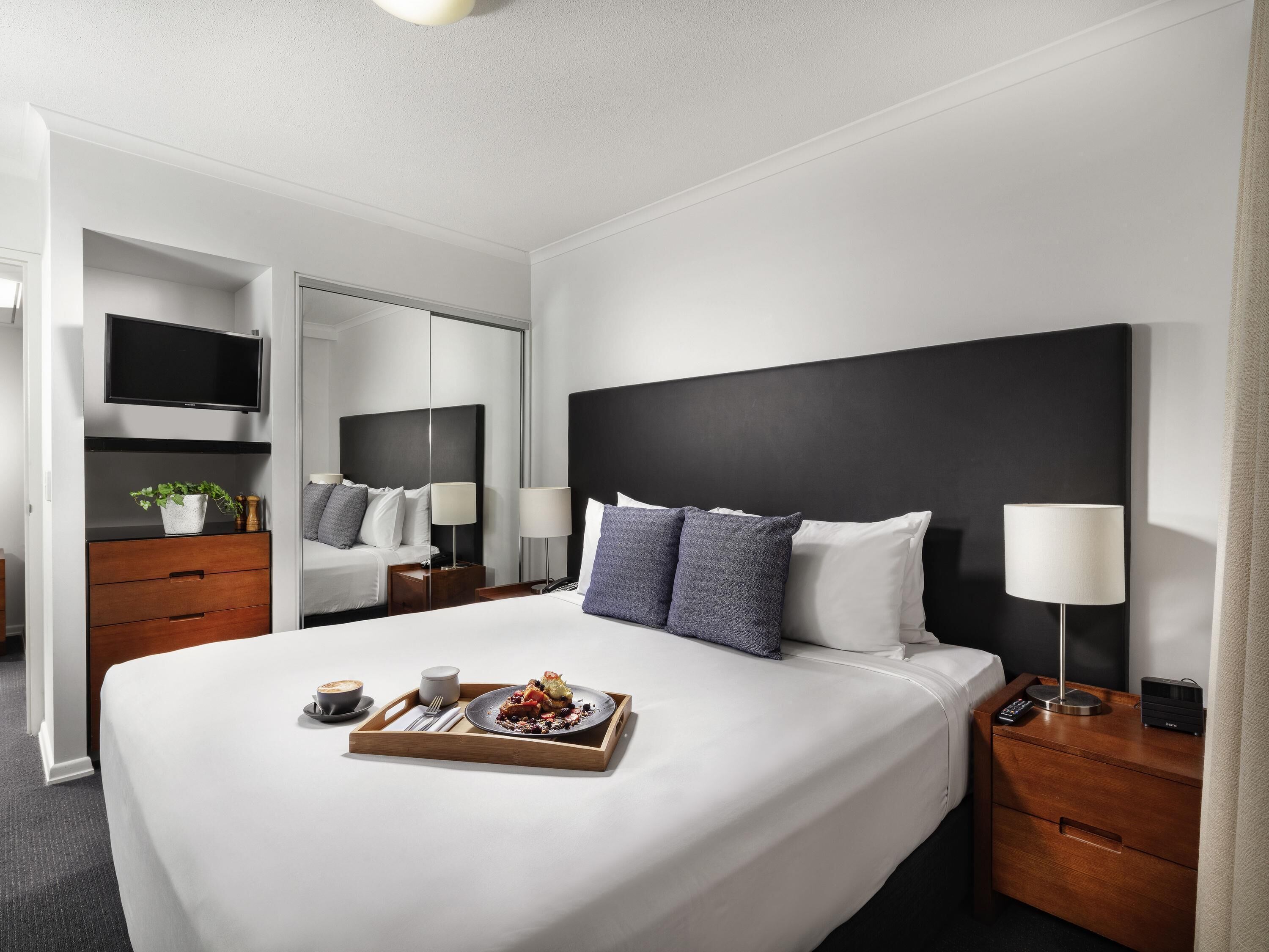A hotel room with a large bed, bedside tables, a TV, and a tray with food.