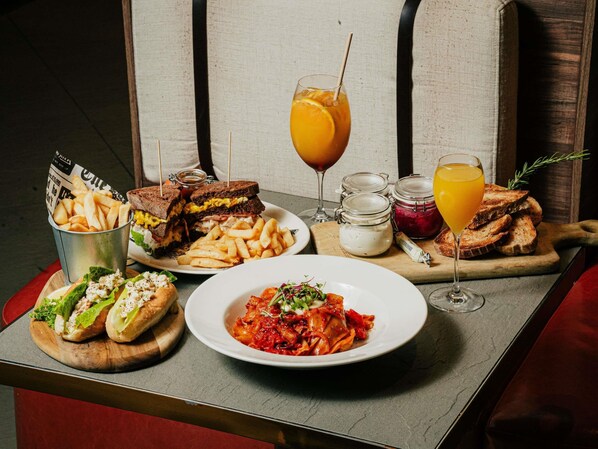A table with a variety of food items including sandwiches, fries, and pasta, along with drinks and condiments. - The Sebel Brisbane (Brisbane)