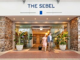 La entrada del hotel The Sebel, con fachada de mármol y plantas en macetas.