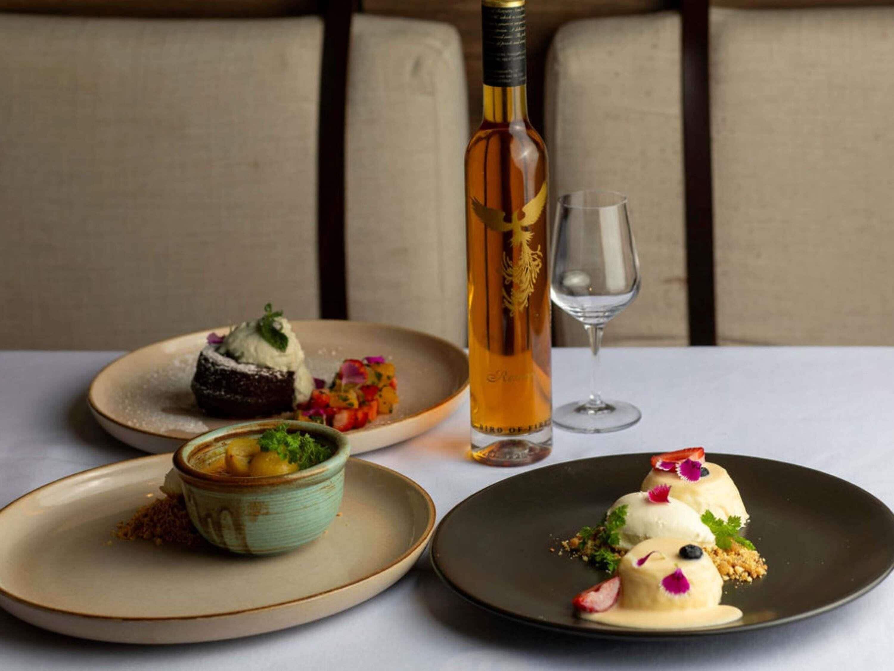 A dining table with three plates of food, a bottle of wine, and a wine glass.