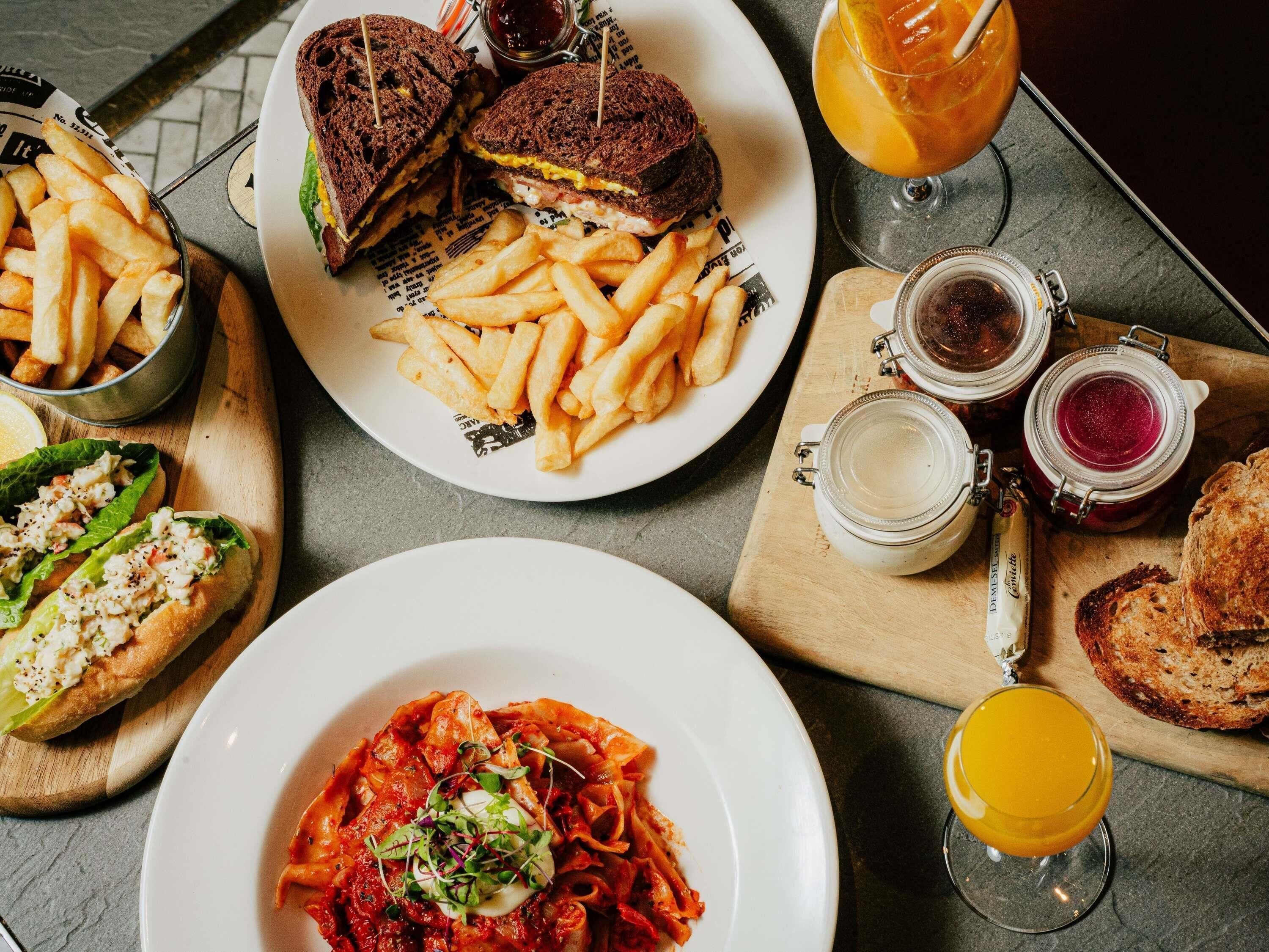 A variety of food items including a sandwich, fries, pasta, and drinks on a table.