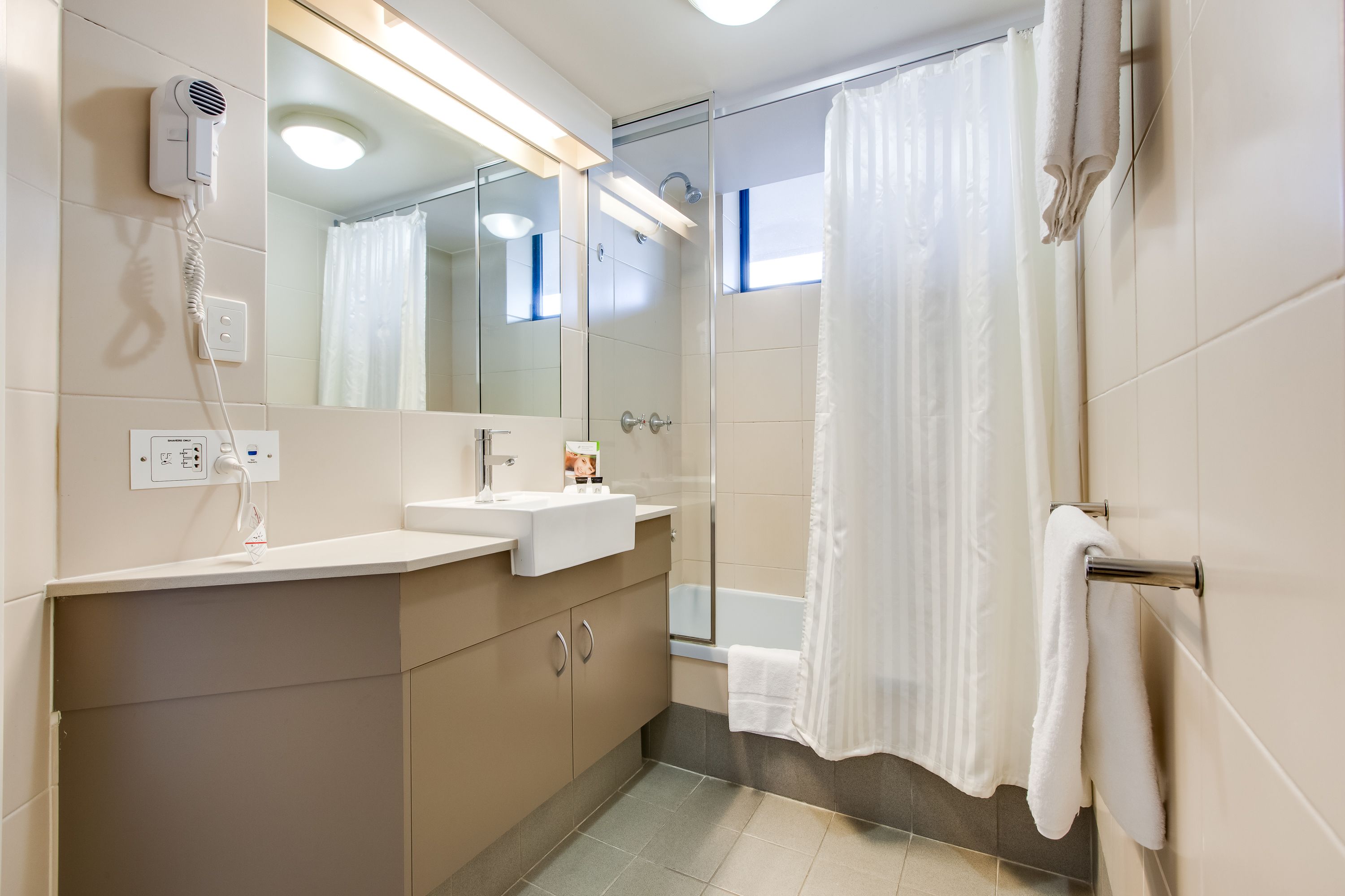 A modern bathroom with a built-in sink, a hair dryer, a mirror, and a shower curtain.