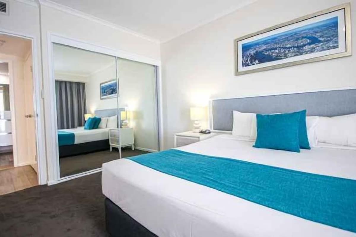 Una habitación de hotel con una cama, una mesita de noche, un espejo y un cuadro en la pared.
