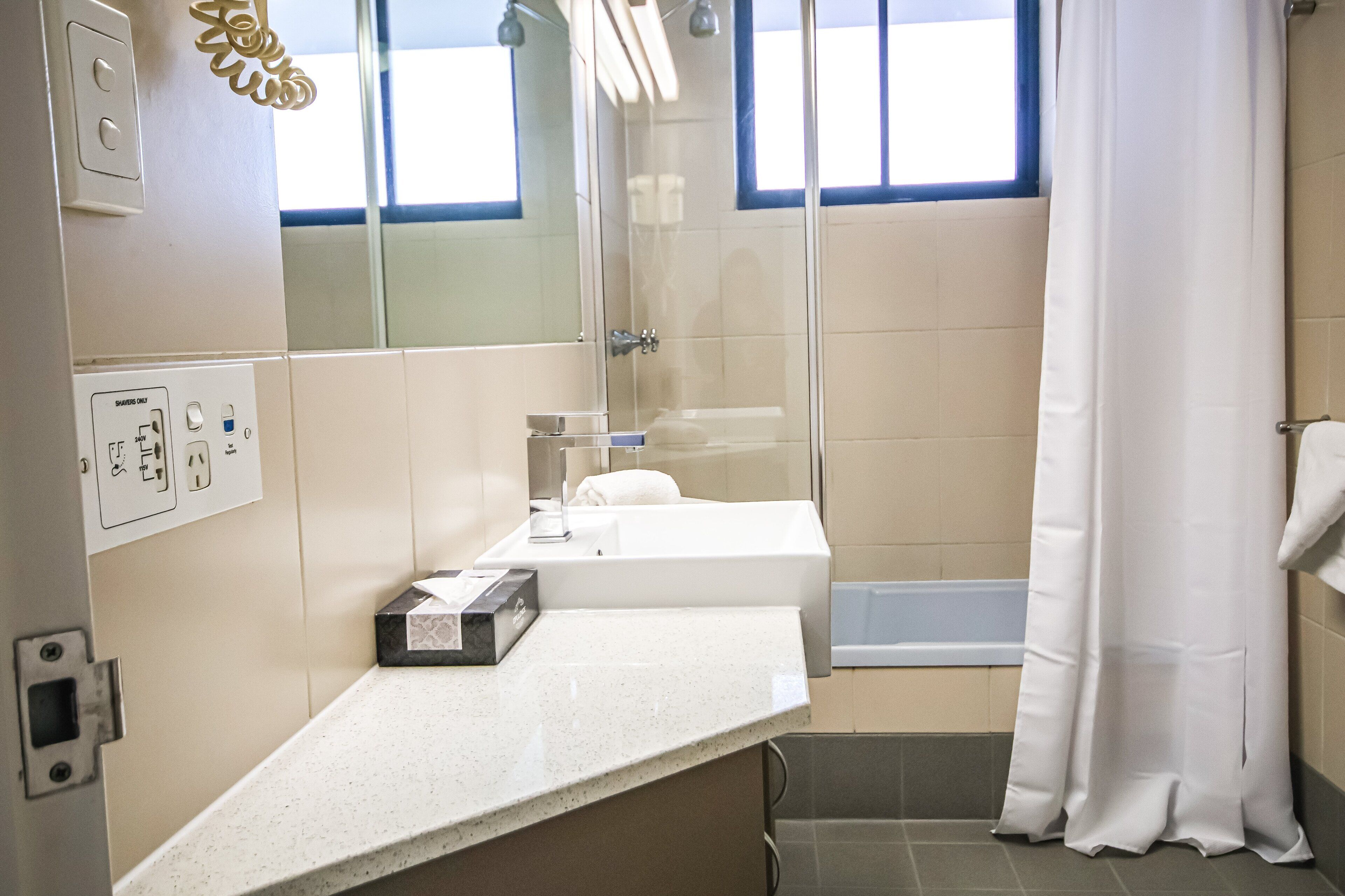 A bathroom with a shower, a sink, a mirror, and a window with a curtain.