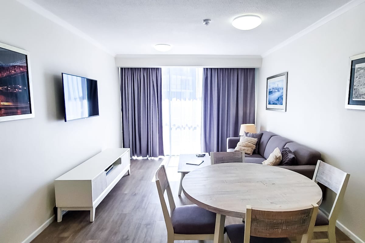 A modern living room with a dining area, a sofa, a TV, and framed pictures on the walls.