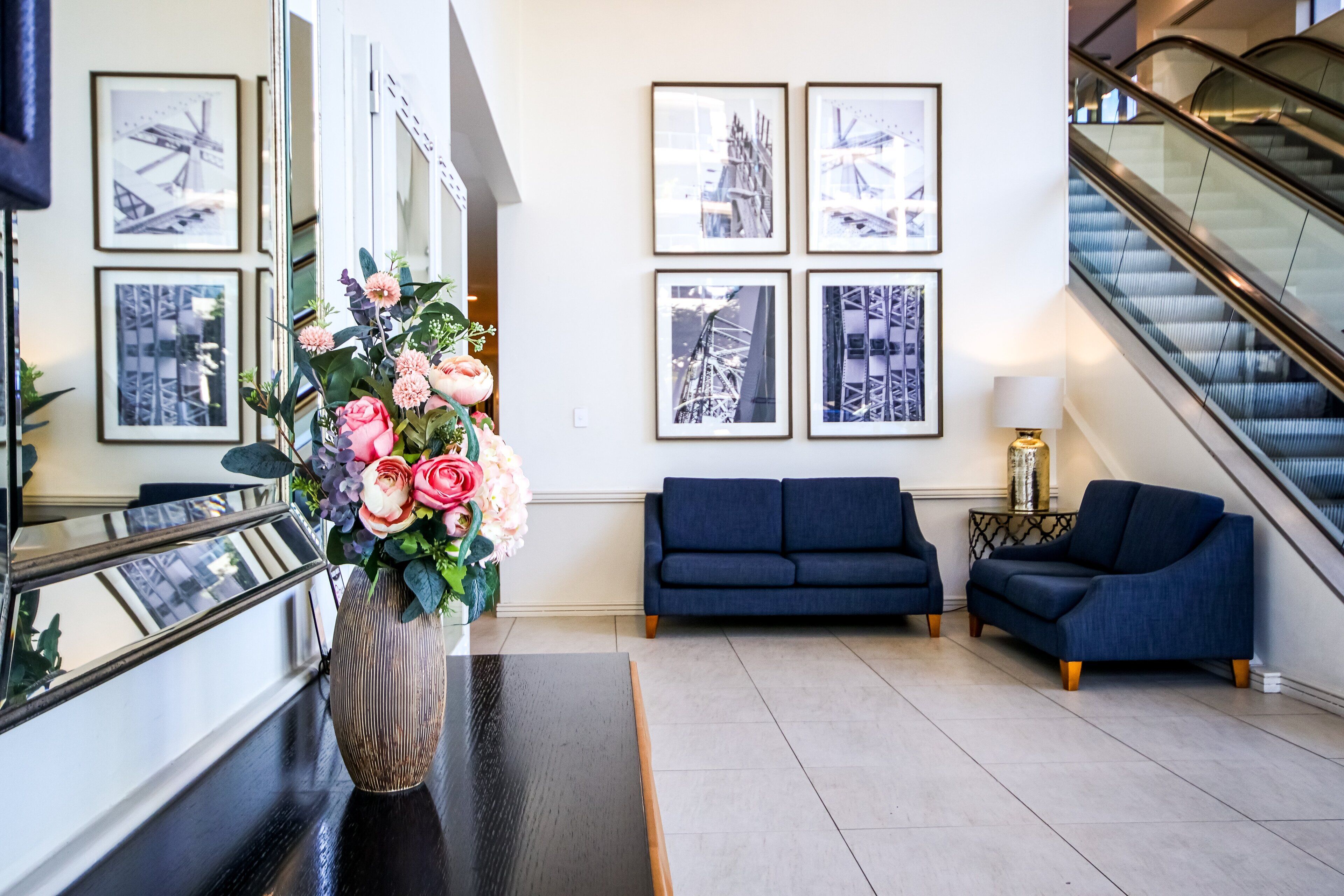 A modern lobby with a dark blue sofa, a vase of pink flowers, and framed pictures on the wall.